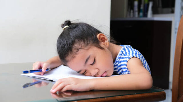 Asian kid sleeping above her textbook showing tiredness