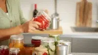 Close up tangan wanita memegang toples kaca dengan makanan yang diawetkan